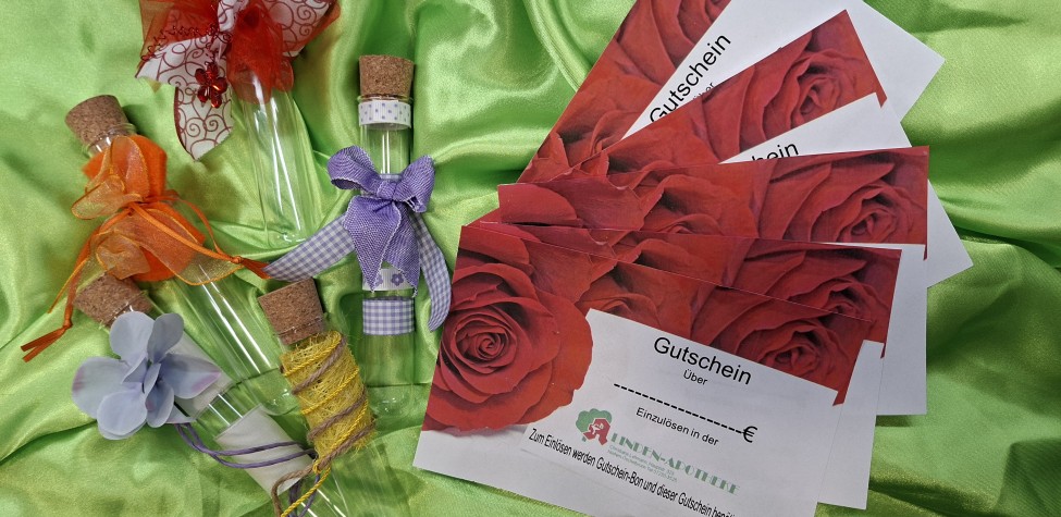 Geschmückte Reagenzgläschen und Gutscheine der Linden-Apotheke Niefern-Öschelbronn auf grünem Stoff