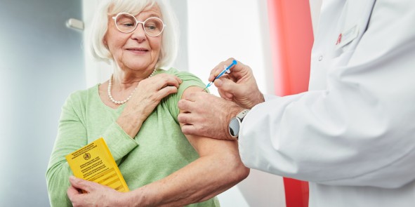 Ein Apotheker verabreicht einer älteren Dame, die ihren gelben Impfpass in der Hand hält, eine Impfung in den Oberarm