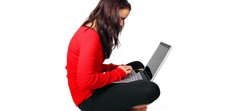 Frau sitzt im Schneidersitz mit einen Laptop auf dem Schoß